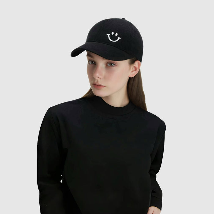 Model wearing Joyful Grin Cap in black, displays iconic smile graphic on a versatile, minimalist streetwear staple.