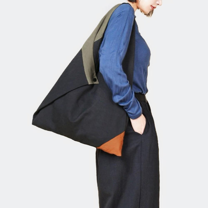 Model wearing the black triangle tote bag over the shoulder; minimalist urban utility look for daily commute.