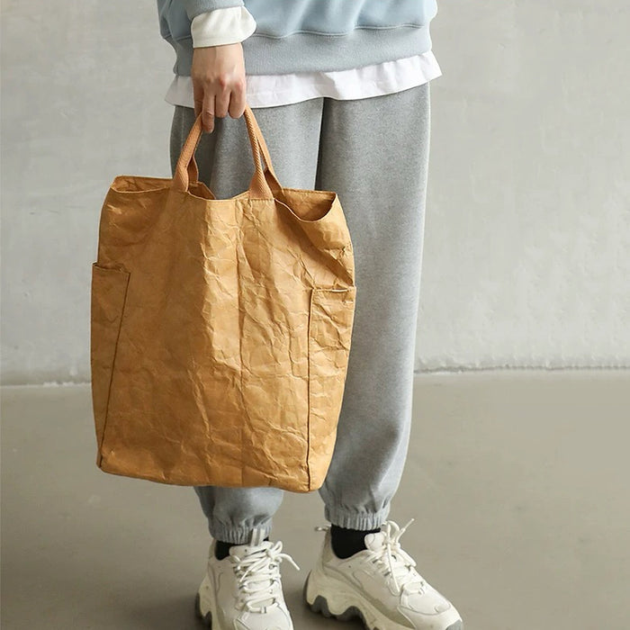 A person holding a tan kraft-paper-textured tote bag, showcasing a modern industrial fashion look.