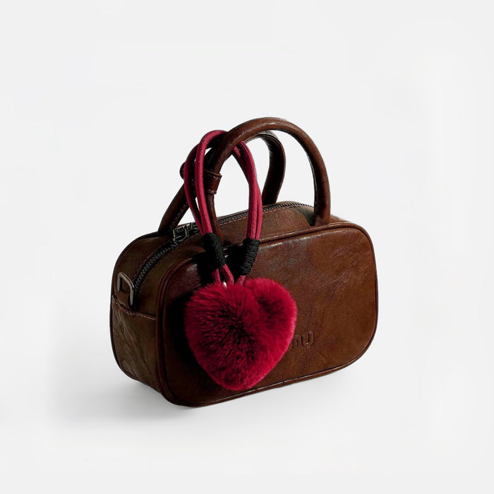 A red love fluff bag charm on brown handbag, great for chic looks and travel days.