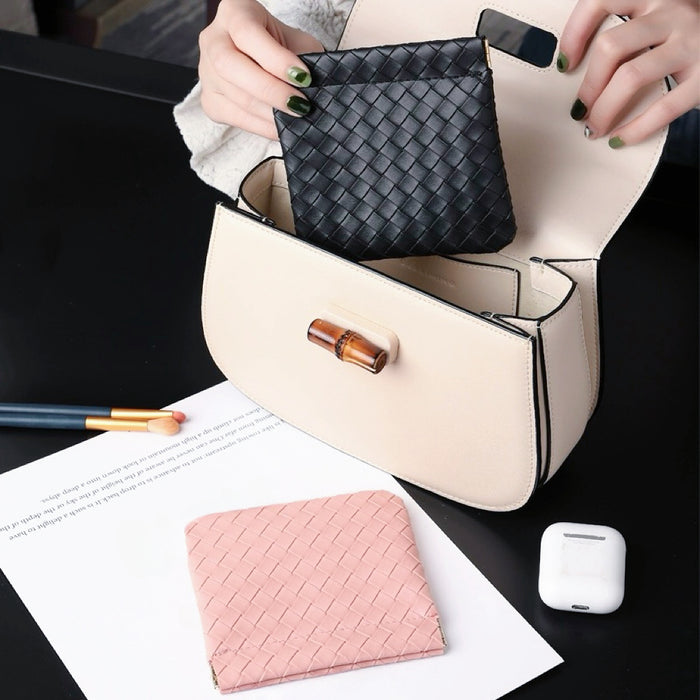 Hands holding black magnetic self-closing storage bag above handbag; woven-texture pouch for makeup and essentials.