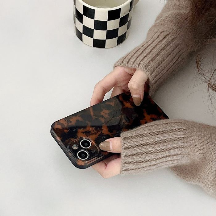 Hand in beige sweater holding Maillard Amber case. Warm tortoiseshell finish for cozy autumn fashion.