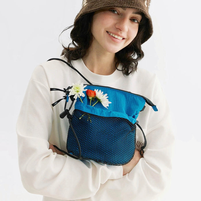 Model carrying a blue nylon crossbody bag handheld, great for daily carry and travel.