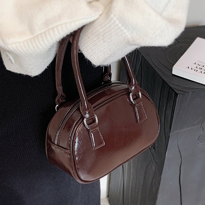 Angled view of umber PU leather mini bowling bag with grab handle and zip-top fastening .