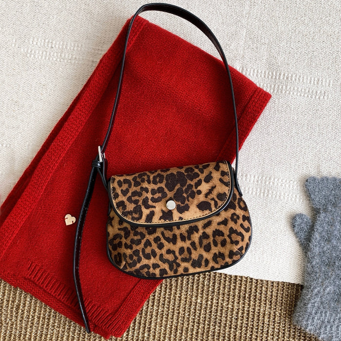 Angled view of Mini leopard print vegan suede saddle bag with black strap and magnetic flap.