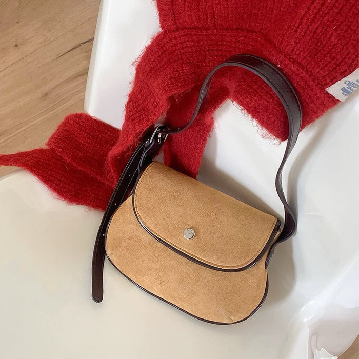 Front view of the khaki mini suede saddle bag on a clean background beside a red sweater.