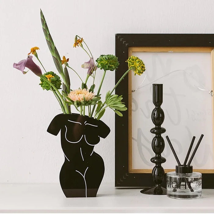 Front view of Black abstract torso vase with colorful flowers on a white shelf, modern decor accents.