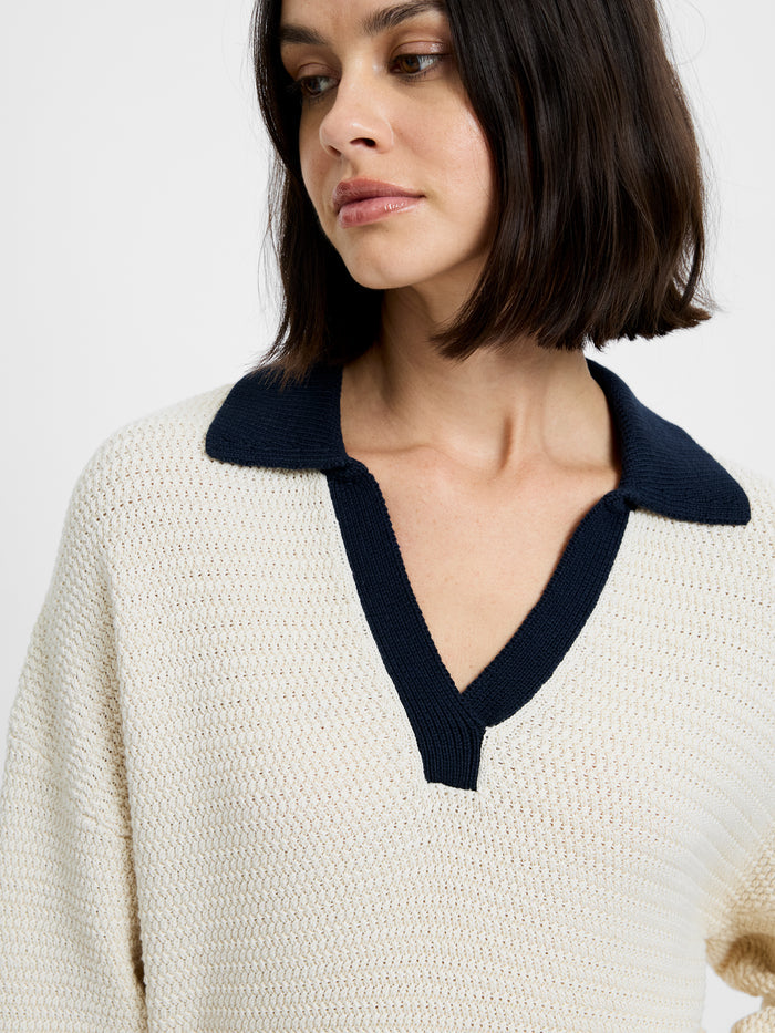 Woman wearing a cream sweater with a navy collar against a white background