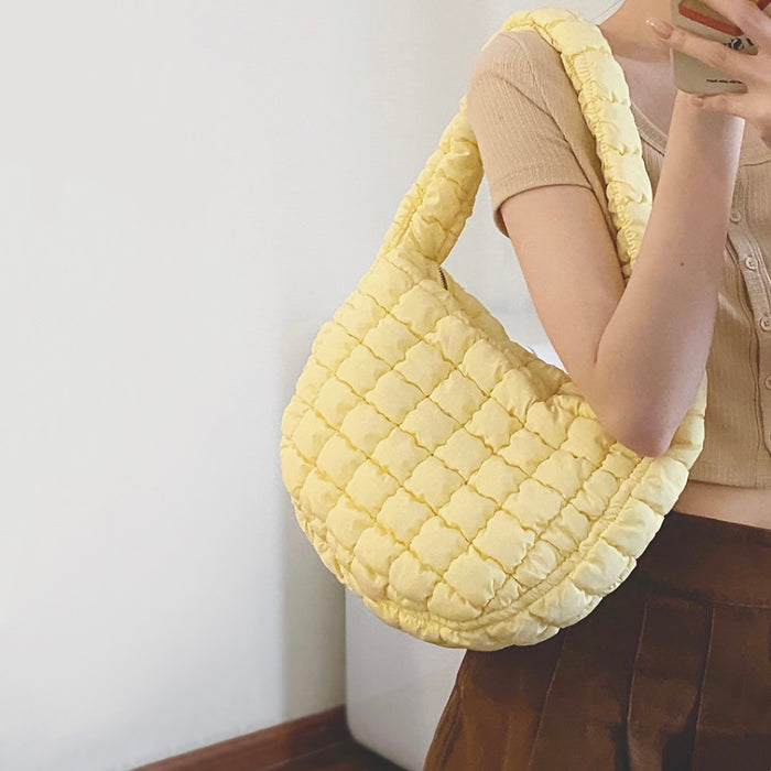 Side view of a model carrying the yellow puffy bag on her shoulder, showing its depth.