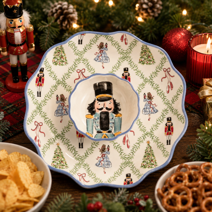A ceramic holiday serving bowl with a matching platter, decorated with nutcracker and Christmas tree motifs, styled on a rustic wooden table with snacks and festive decorations.