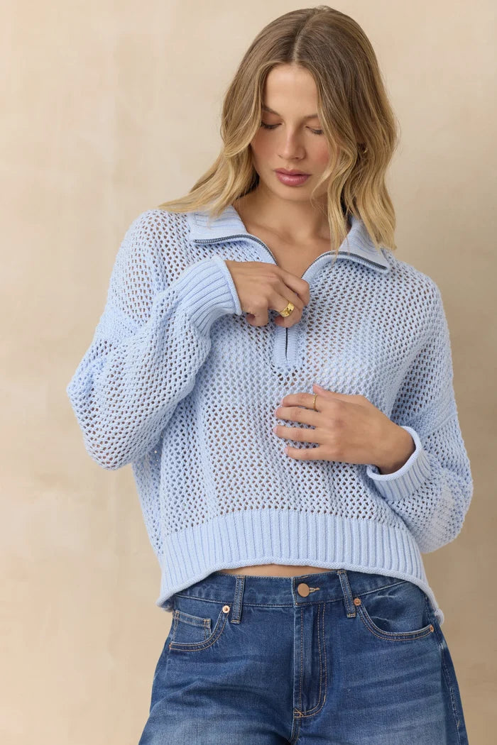 Woman wearing a light blue knitted sweater and blue jeans against a beige background