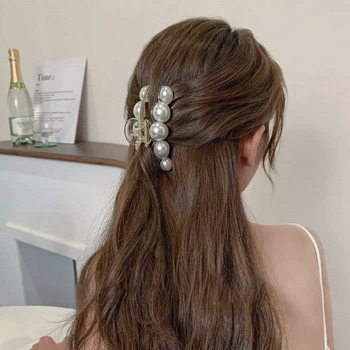 Model styling an oversized pearl hair claw in a half-up bun; trendy hair clip for romantic wedding guest looks.