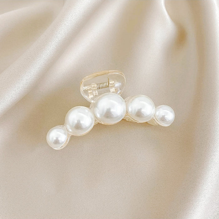 Side view of a curved pearl hair claw on satin; highlighting the high-luster pearls and lightweight ABS material.