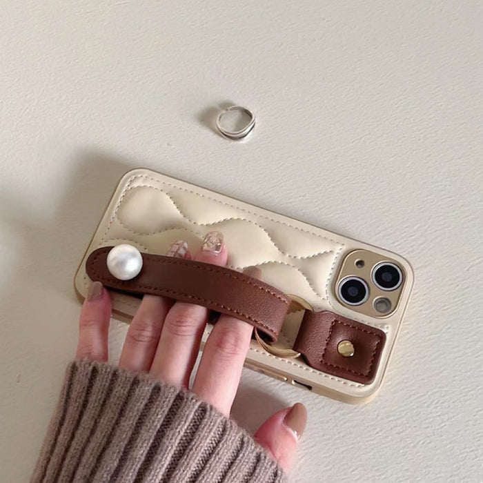 Cream quilted leather case featuring a large pearl accent and brown wrist strap.
