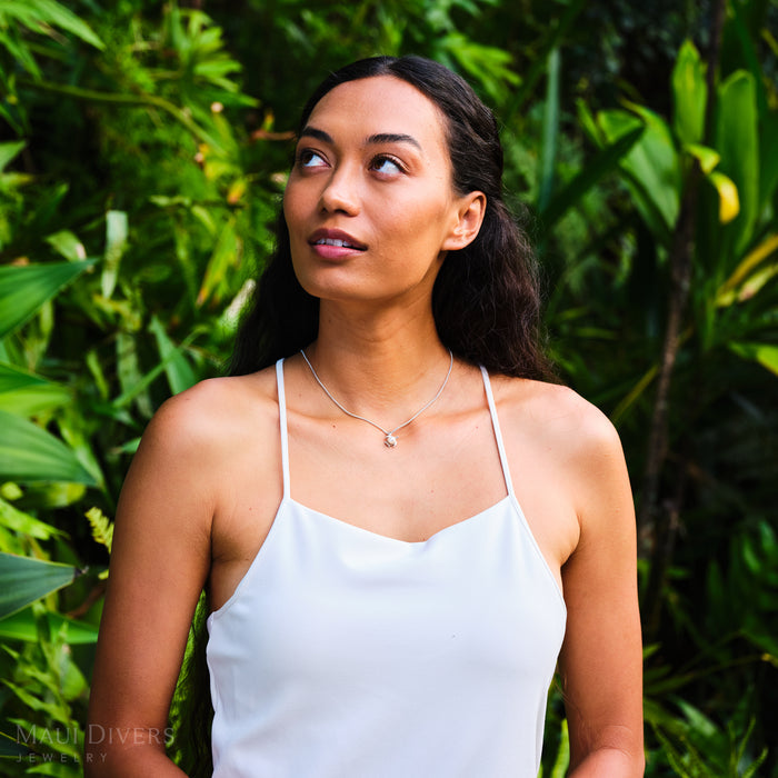 Woman wearing a white top and a Honu Pendant in Sterling Silver with a White Pearl with a green leafy background