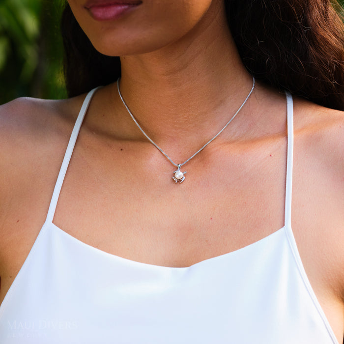 Woman wearing a white top and a Honu Pendant in Sterling Silver with a White Pearl with a green leafy background