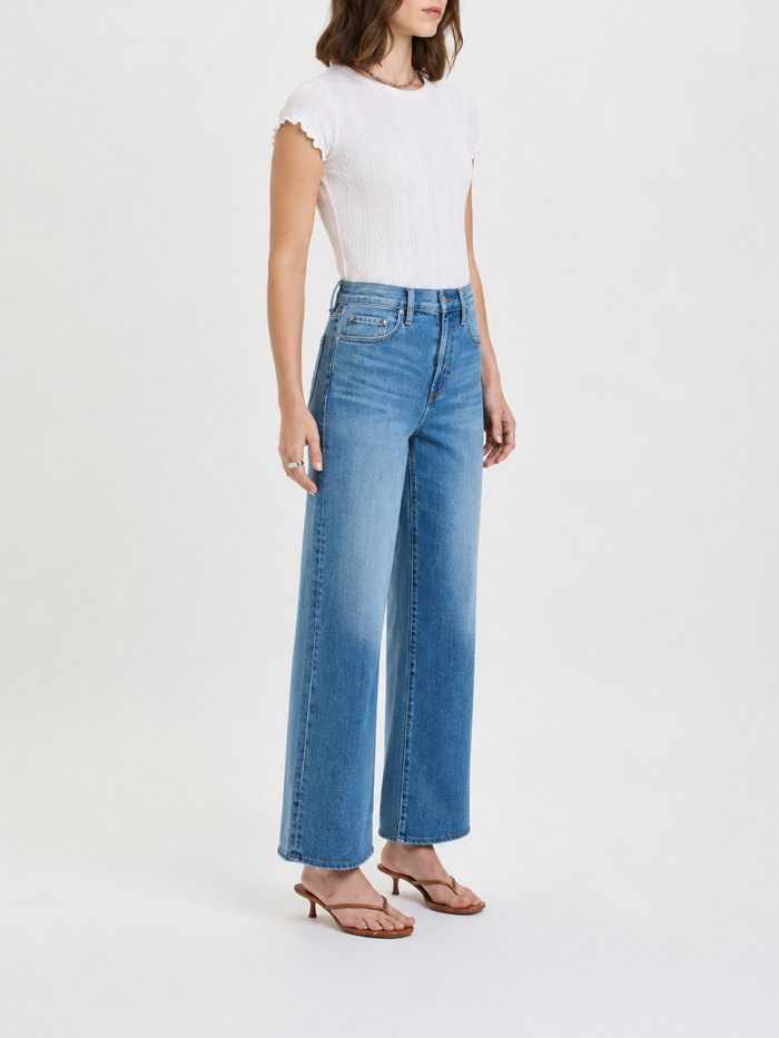 Woman wearing blue jeans and a white top on a white background