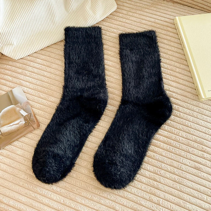 Angled view of black plush cozy socks on a textured beige surface.