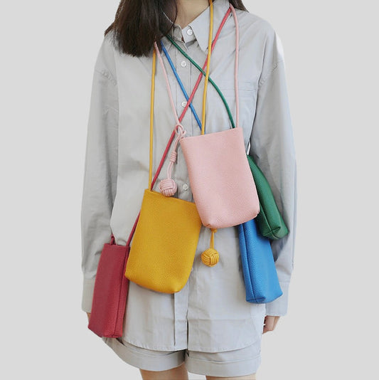 Five colorful hanging ball leather bags in red,  pink, blue, green and yellow, worn together by a person.