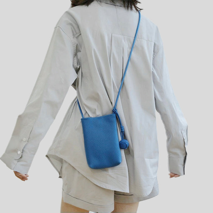 Model carrying a blue Polycolor hanging ball leather bag as crossbody, clean minimalist look.