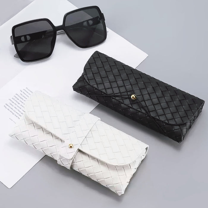 Front view of Black and white woven PU leather glasses cases with gold button closures, beside black sunglasses.