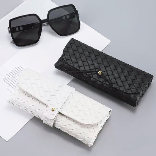 Front view of Black and white woven PU leather glasses cases with gold button closures, beside black sunglasses.