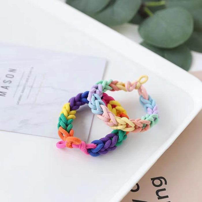 Two braided rainbow elastic hair rings on a white tray.