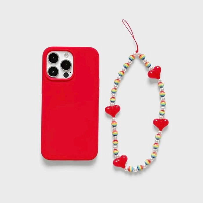 Flat lay of Rainbow Heart Phone Charm beside a red phone case, ideal for travel and daily use.