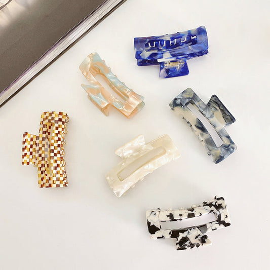 Angled view of six rectangle acrylic hair claws in various marbled colors.