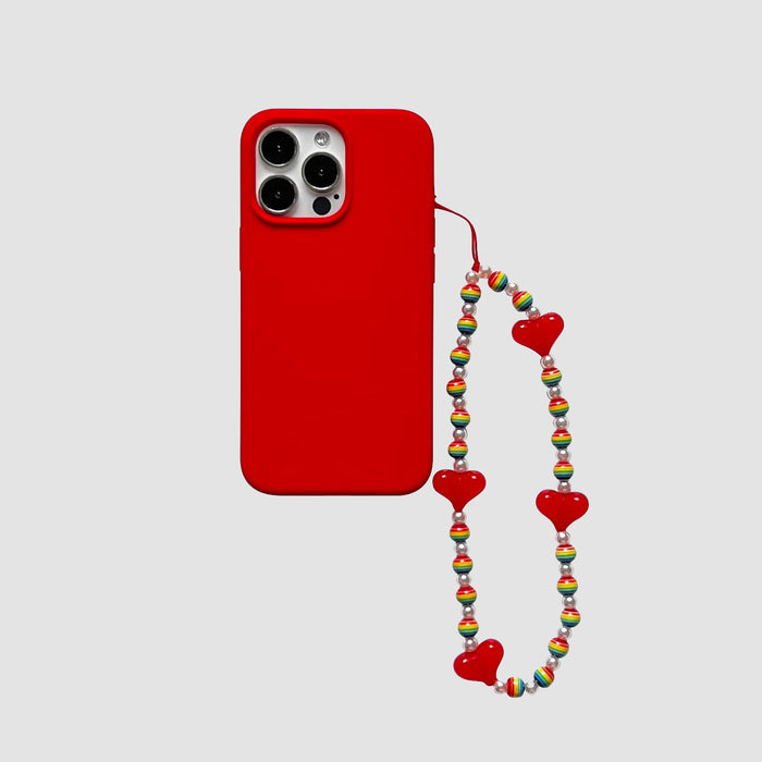 Red silicone iPhone case with a beaded rainbow heart charm. Vibrant Indie aesthetic accessory.