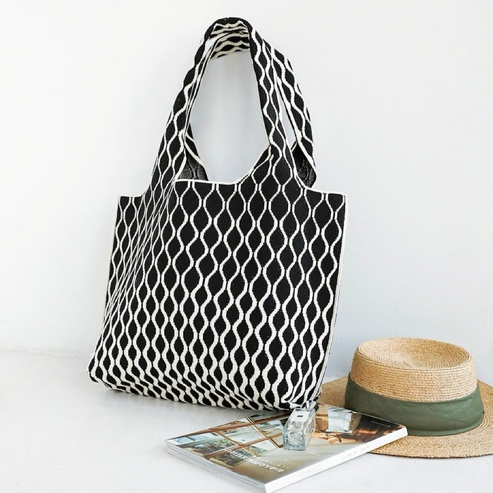 Black and white ripple texture polyester tote bag with wide straps, beside a straw hat.