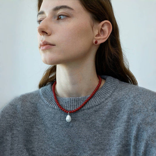 Model wearing red resin bead necklace with artificial pearl drop, elegant jewelry styling
