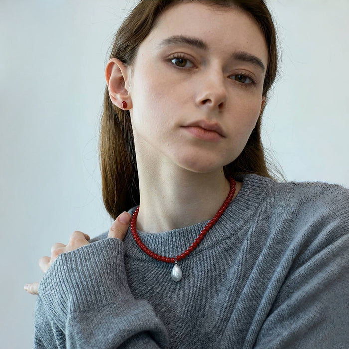 Close up of red bead necklace with pearl pendant on model, showing resin texture
