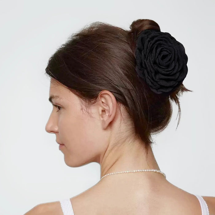 Side view of a model styling a classic black fabric rose hair claw with a pearl necklace.