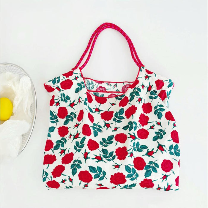Close-up of White polyester tote bag with red rose print, pink grab straps, and inner slip pocket Rose Romance Tote.