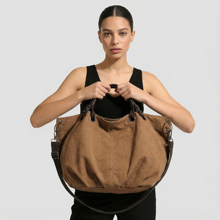 Model holding the brown canvas tote bag by the top handles.