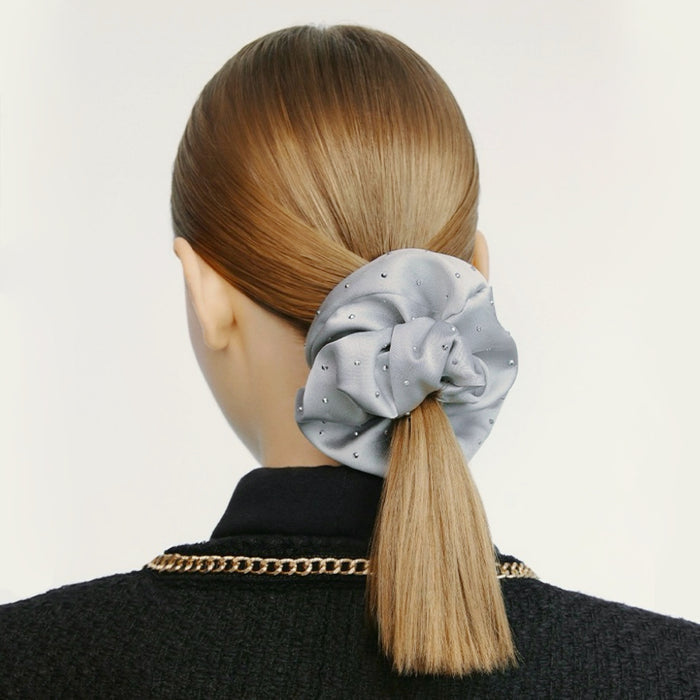 Model wearing a light gray satin scrunchie with rhinestones on a blonde ponytail.