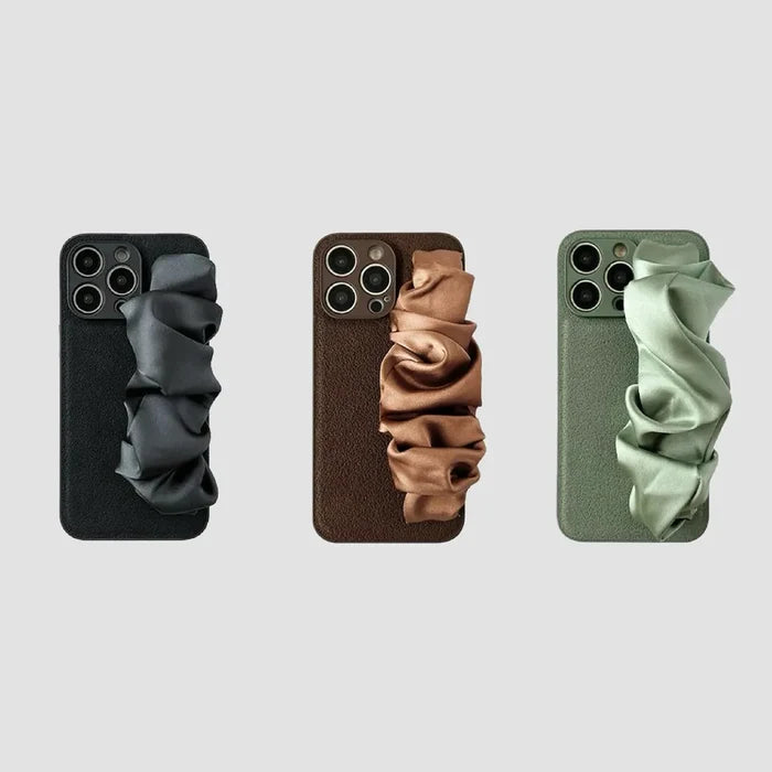 Three silicone iPhone cases with black, brown, and olive green satin scrunchie wristbands.