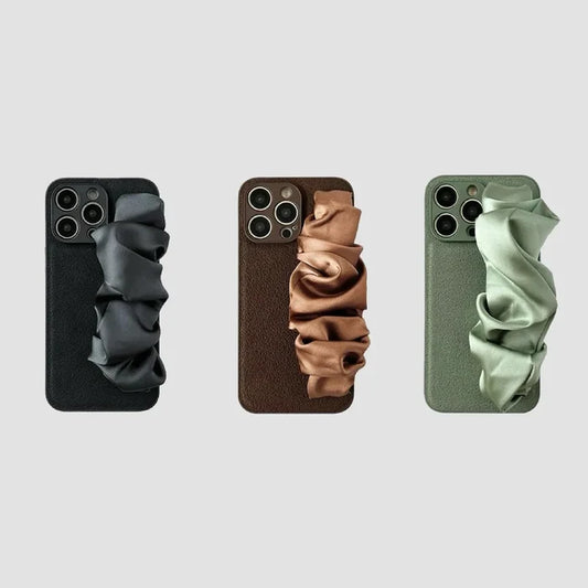 Three silicone iPhone cases with black, brown, and olive green satin scrunchie wristbands.