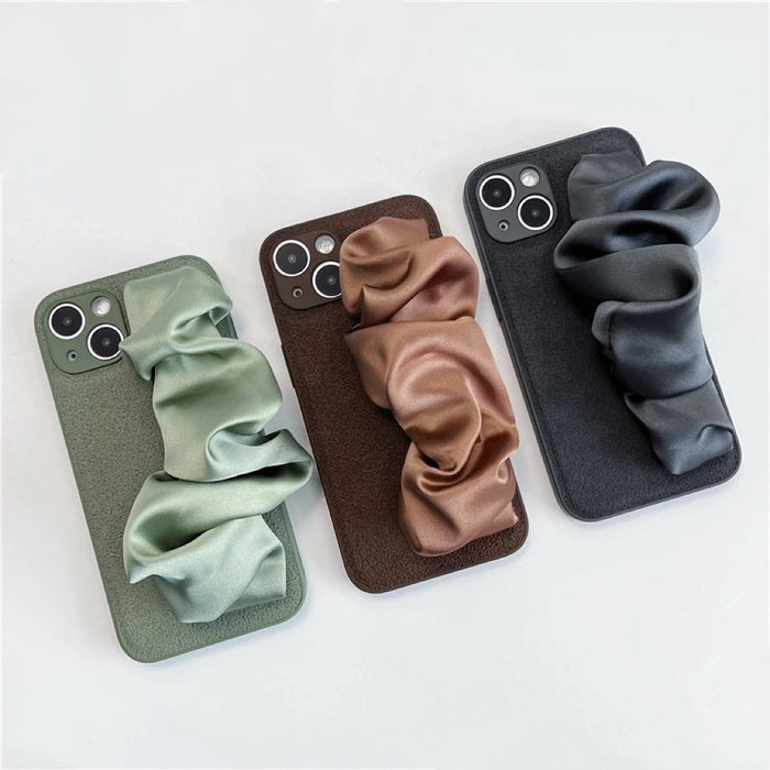Three silicone cases with sage green, brown, and dark gray satin wristbands. Luxury textures.