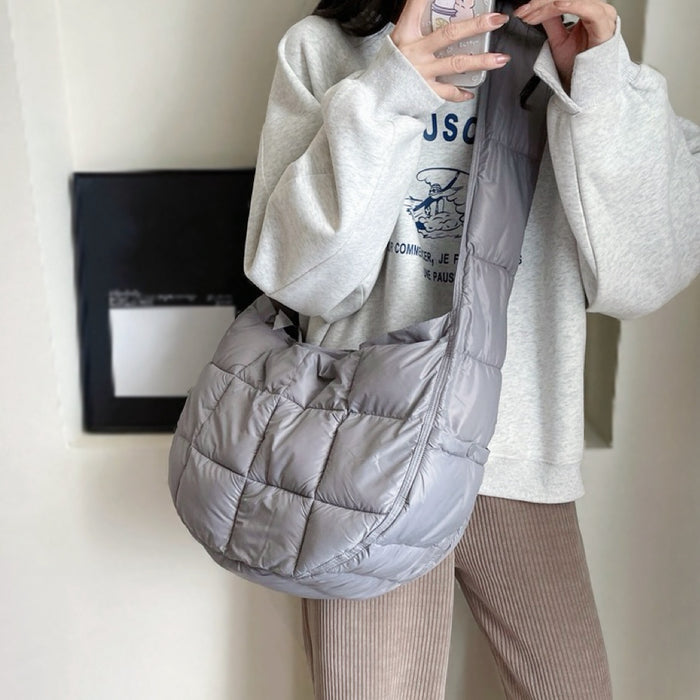 Model wearing a large grey padded crossbody bag; lightweight puffer sling bag for urban commute.