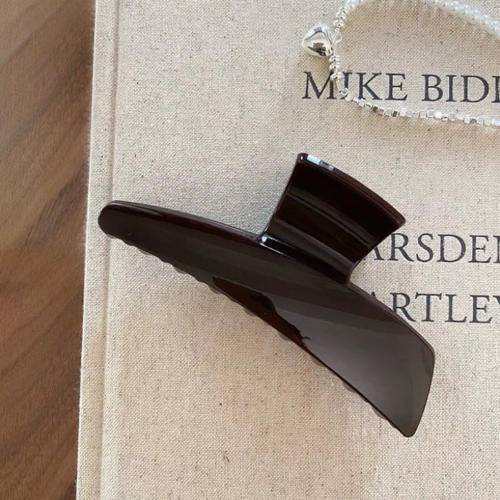 Flat lay of Sleek Curved Hair Claw  in dark brown, great for everyday styling and gifting.