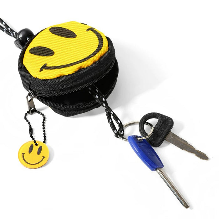 Smiley coin purse beside keys; round yellow zip pouch with black lanyard and charm for coins, earbuds, or tags.