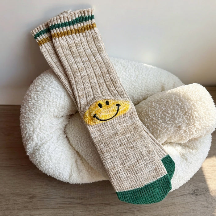 Khaki knit ribbed crew socks with a yellow embroidered smiley face patch.