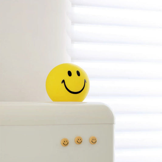 Angled view of Bright yellow polyethylene smiley face piggy bank ornament on a white surface.