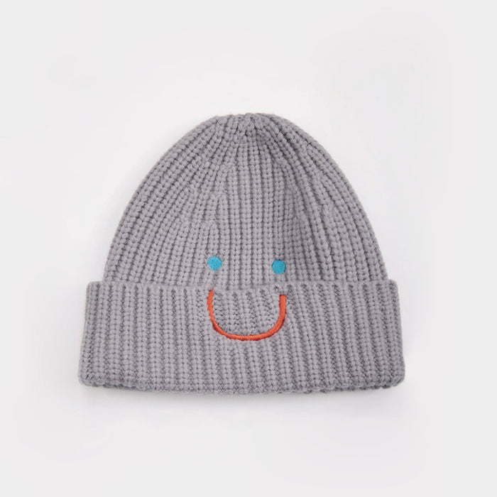 Gray ribbed knit beanie with an embroidered blue-eyed smiley face, adding a playful touch to winter gear.