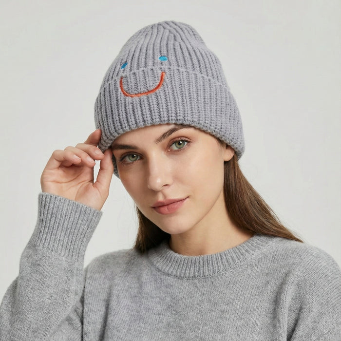 Woman wearing a gray ribbed knit beanie with a fun embroidered smiley face for a trendy casual style.