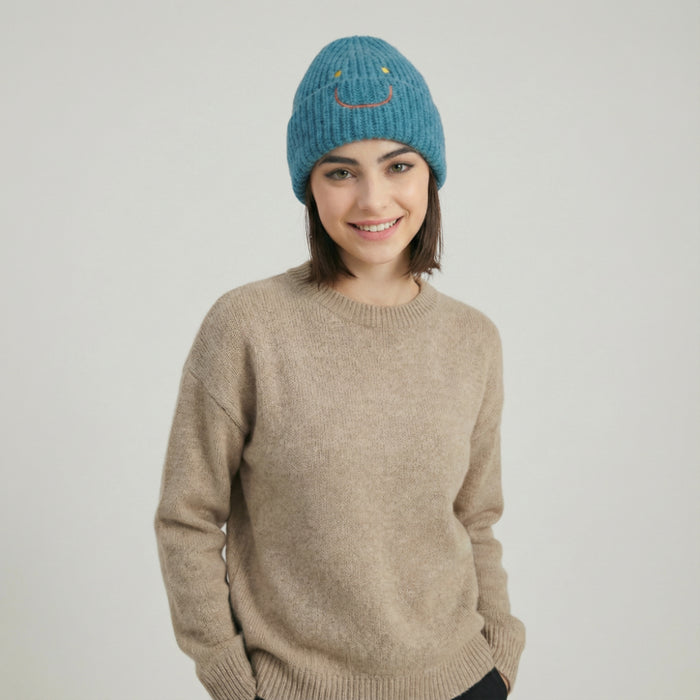 Model wearing Smiley Ribbed Knit Beanie in peacock blue. Stylish head protection for urban winter outings.