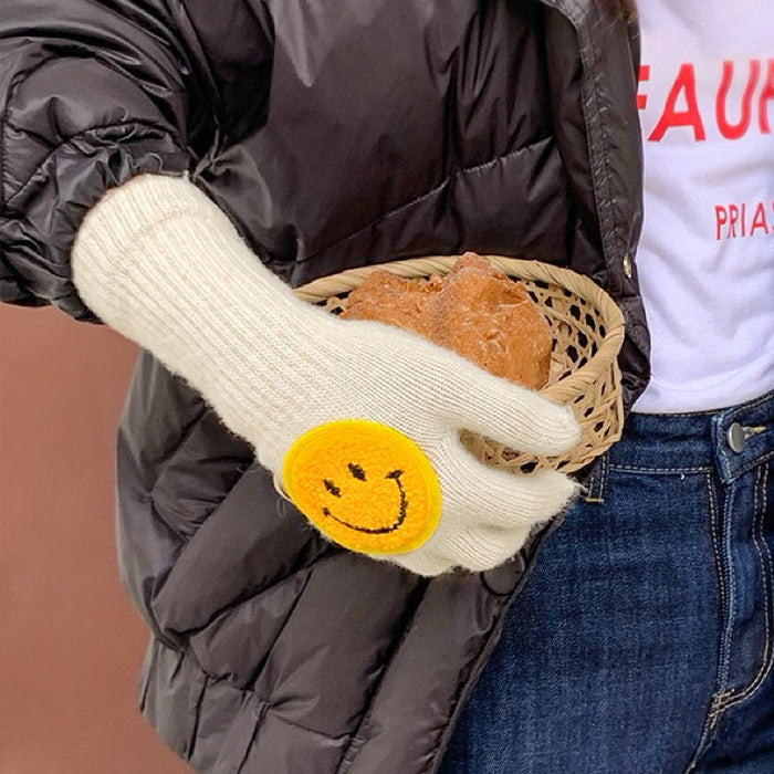 Model wearing smiling round face gloves in white, plush knit with smile patch; cute warmth for winter days.