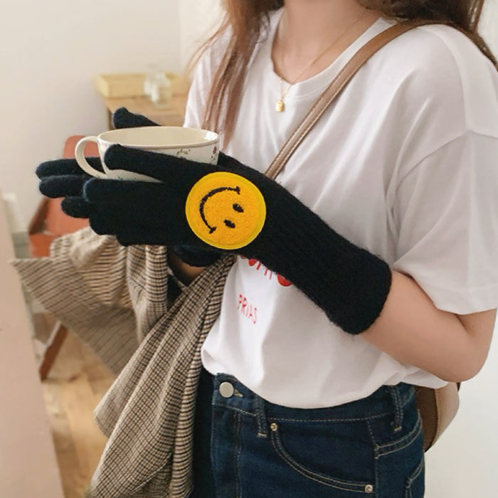 Black smiling round face gloves with plush knit texture and smile patch, flat lay; cozy winter accessory.